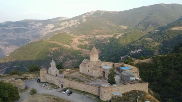 Tatev monastery complex sits atop a lush, green hill in Armenia, surrounded by rugged mountains and expansive valleys.