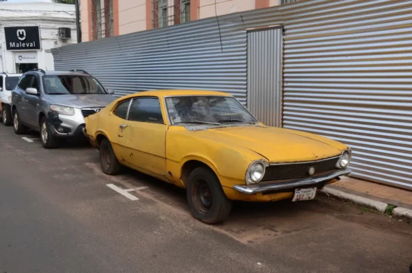 Vintage yellow car parked on a street in Villarica, Paraguay, alongside modern vehicles and a metallic fence.