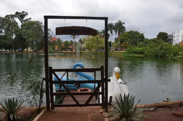 Vibrant view of a serene lake in Villarica, Paraguay, featuring a dock with a swan-shaped boat and lush greenery.