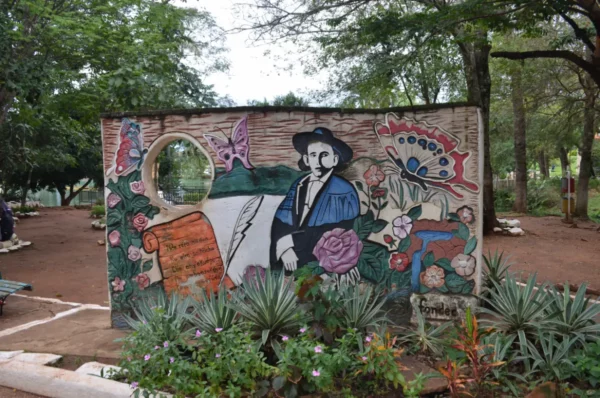 Colorful mural depicting a historical figure surrounded by flowers and butterflies in Villarica, Paraguay's lush outdoor park.