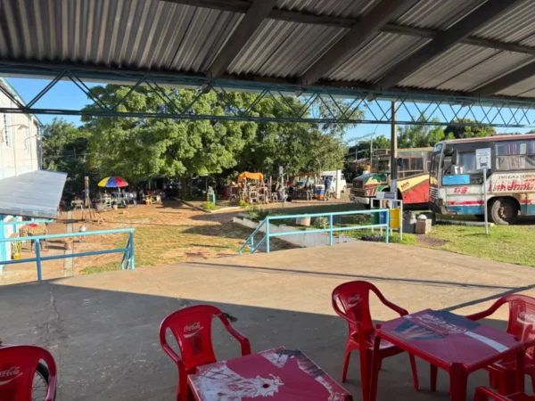 Bright red chairs and tables on a concrete patio overlook a bustling market scene in Villarica, Paraguay, with greenery and colorful vendors.