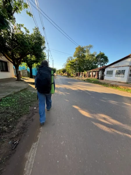 A traveler walks along a quiet street in Villarica, Paraguay, surrounded by greenery and clear blue skies.