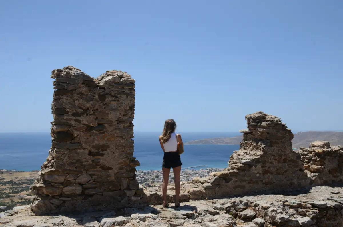 girl staring at view of blue sea and sky in karystos from between battlements of castello rosso medieval castle