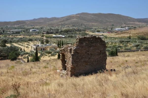 Ruined stone structure stands amid dry grass and olive groves, set against rolling hills in Karystos, Euboea, Greece.