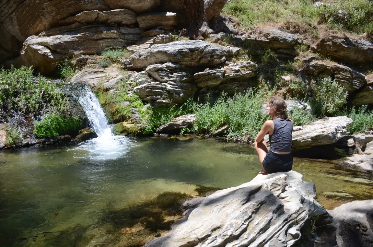 girl sitting on rock and staring at waterfall In Dimosaris Gorge