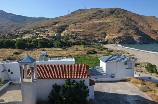 Potami Beach in Euboea features sandy shores and green hills, with white buildings and a blue sky in the background.