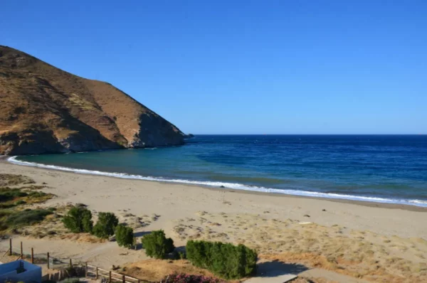 Potami Beach features golden sands, serene blue waters, and gentle hills of Euboea, Greece under a clear blue sky.