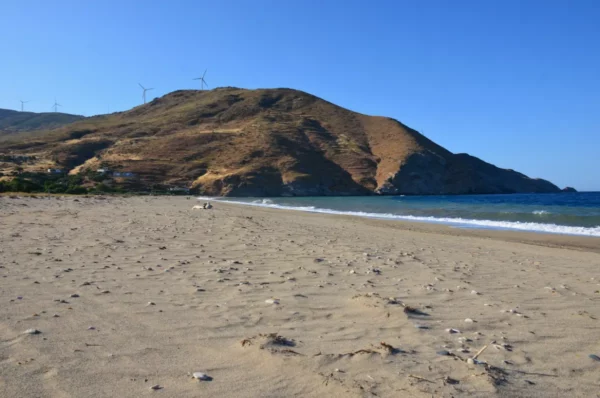 Golden sands stretch along Potami Beach, Euboea, Greece, with gentle waves lapping the shore and distant hills in the background.