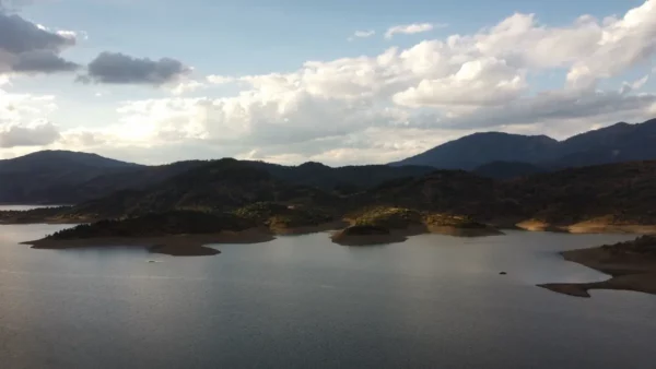 Serene Aoos Lake in Ioannina, Greece, surrounded by lush hills and dramatic clouds under a clear sky.