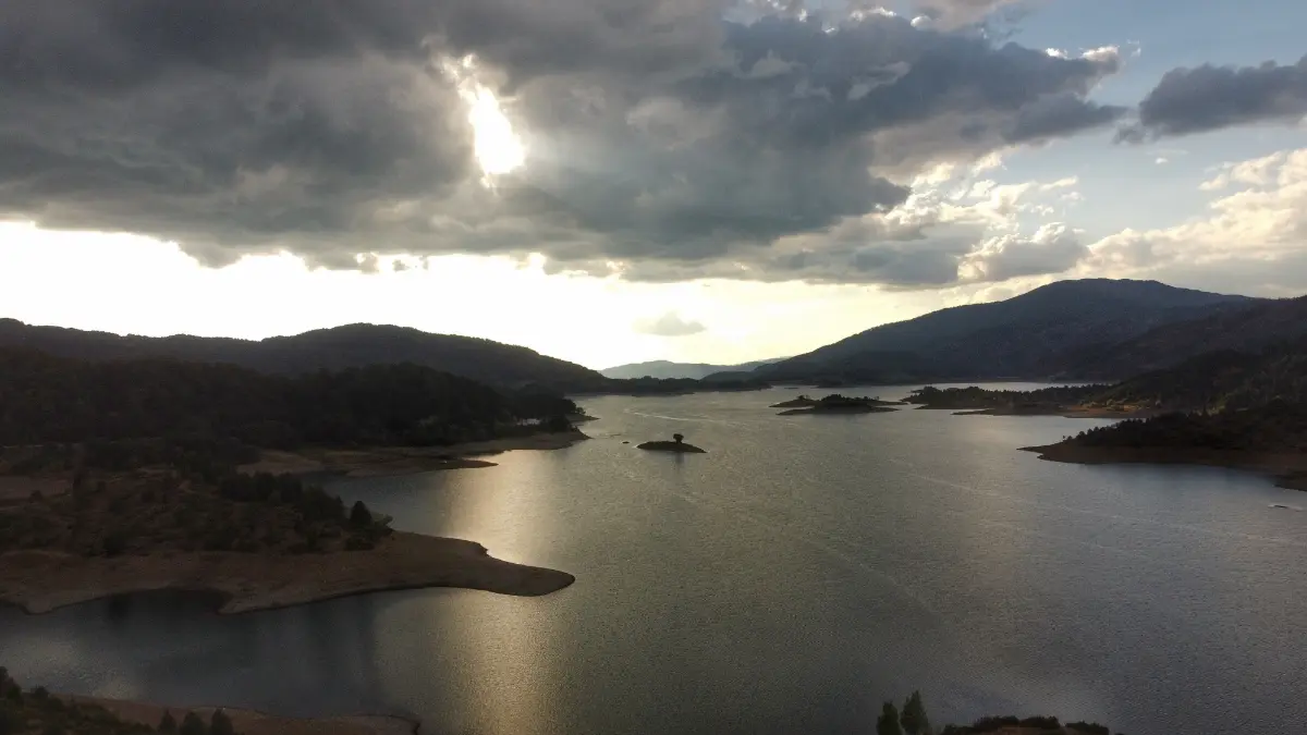 Stormy sky over Aoos Springs Lake, sun rays breaking through dark clouds and reflecting on the calm water, Epirus, Greece