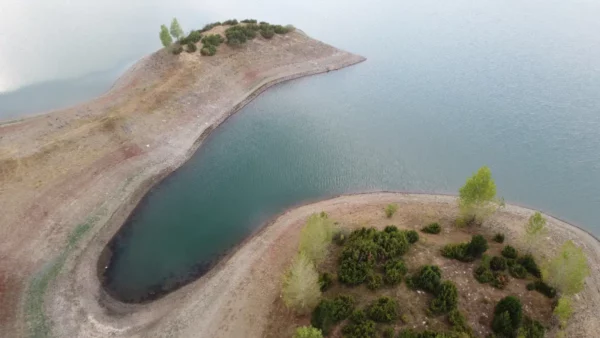 Serene view of Aoos Lake featuring green patches and sandy shores, showcasing the natural beauty of Ioannina, Greece.