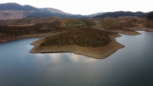 Aoos Springs Lake with winding shoreline and small peninsulas, calm blue water reflecting clouds, surrounded by rugged hills in northern Greece