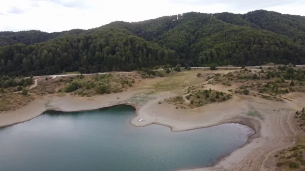 Serene view of Aoos Lake surrounded by lush greenery and mountains in Ioannina, Greece, showcasing tranquil waters and sandy shores.