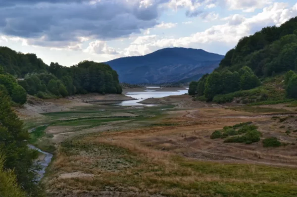 Stunning view of Aoos Lake's serene landscape in Ioannina, Greece, featuring lush greenery and distant mountains under a cloudy sky.