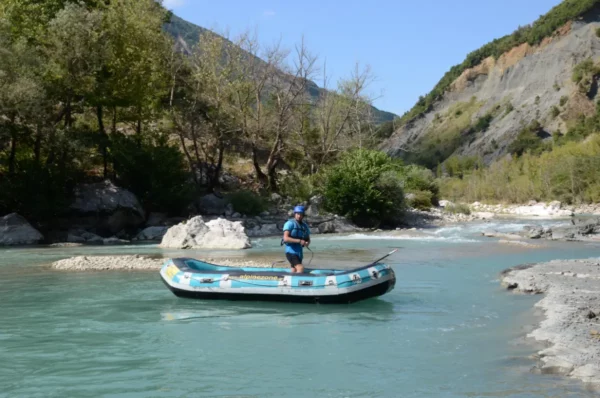 A person stands in a blue raft on the turquoise Arachthos River, surrounded by lush greenery and rocky hills in Ioannina, Greece.