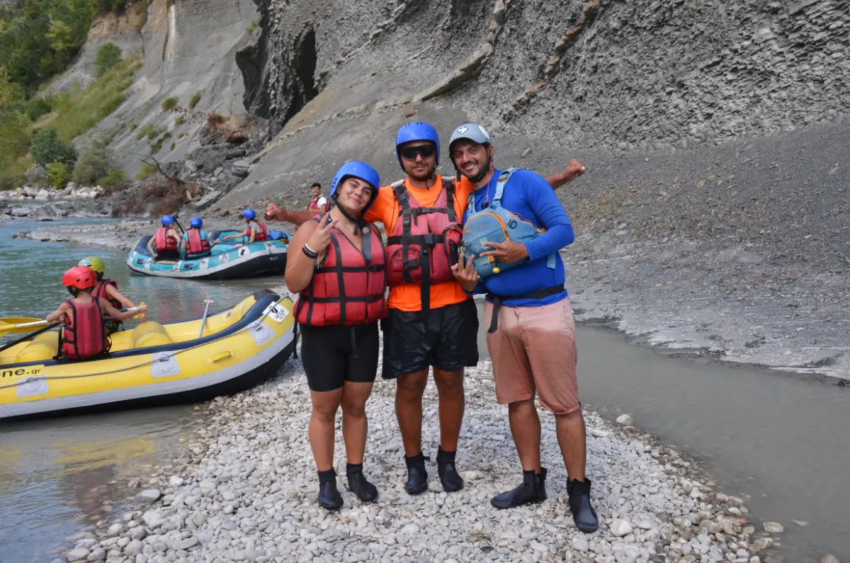 Three rafters posing with their guide on the rocky bank of the Arachtos River in Tzoumerka, Greece