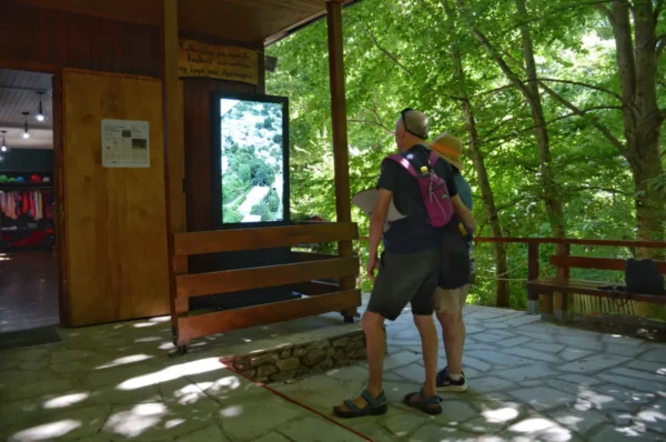 Visitors explore interactive displays at the Arcturos Bear Conservation Area in Florina, Greece, surrounded by lush greenery.