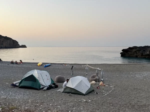 Tents set up on the sandy shore of Chiliadou Beach in Euboea, Greece, with calm waters and soft pastel skies at dusk.
