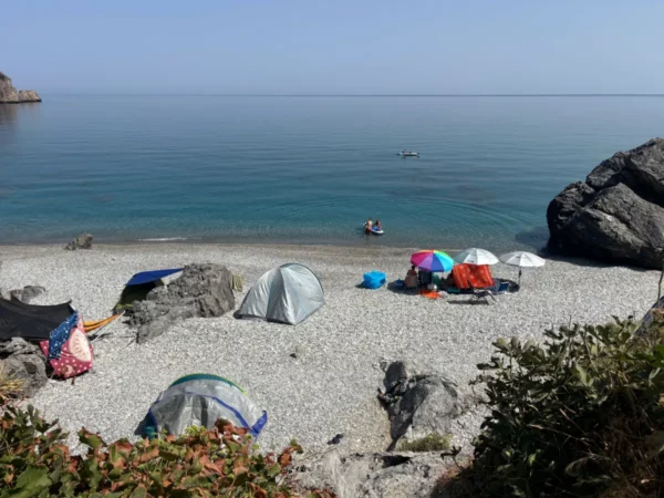 Colorful tents dot the pebbled shore of Chiliadou Beach, Euboea, Greece, with calm waters and bright blue skies above.
