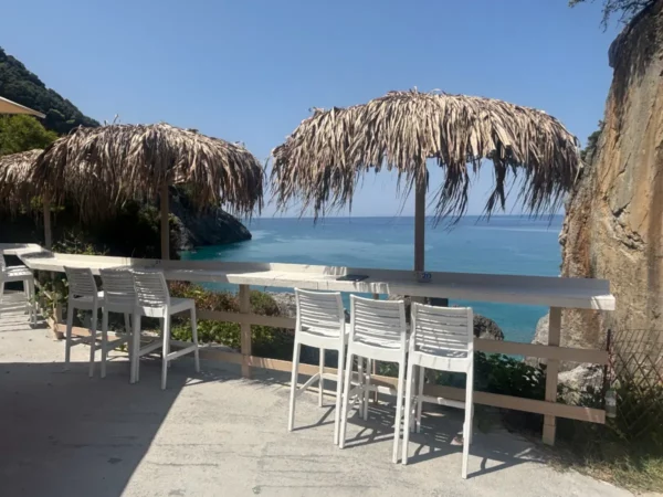 Chiliadou Beach in Euboea features straw umbrellas and white chairs overlooking serene blue waters and rocky cliffs.