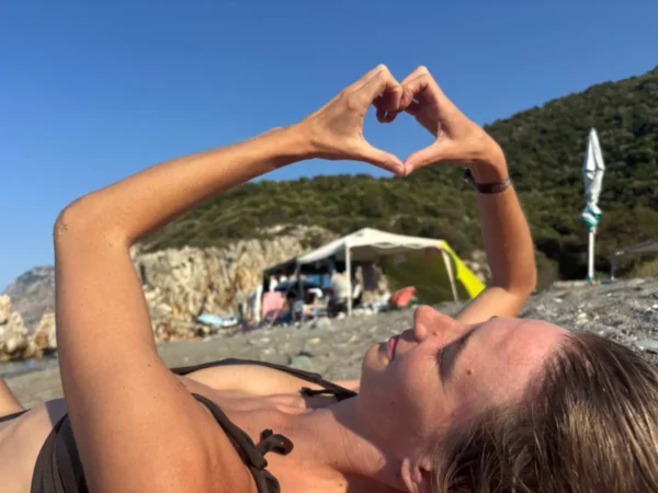 Creating a heart shape with her hands, a woman relaxes at Chiliadou Beach, Euboea, Greece, under a bright blue sky.
