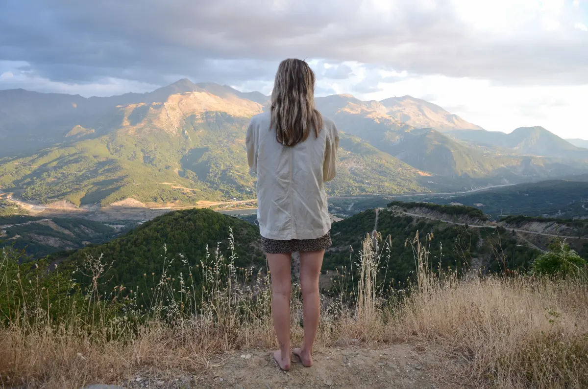 Woman standing on a ridge overlooking Mount Lakmos and the Aoos valley at sunset, Epirus, Greece