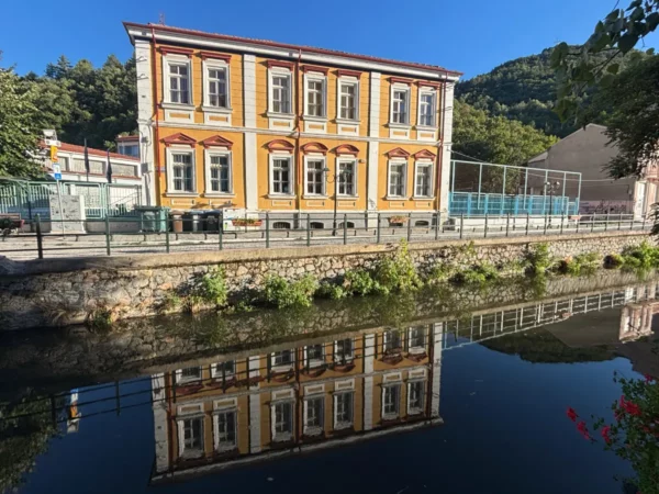 Colorful historic building with classic architecture reflecting in the calm waters of a canal in Florina, Greece.