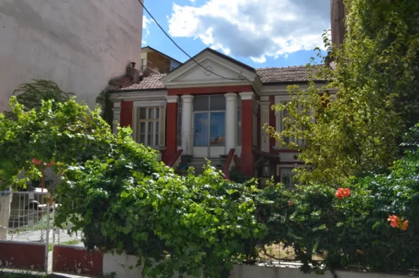 Colorful architecture framed by lush greenery in Florina, Greece, showcasing a charming building with classic columns and vibrant flowers.