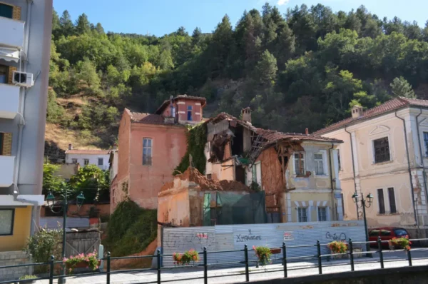 Charming old buildings, partially collapsed, with greenery on a hillside backdrop in Florina, Greece. Renovation efforts visible.