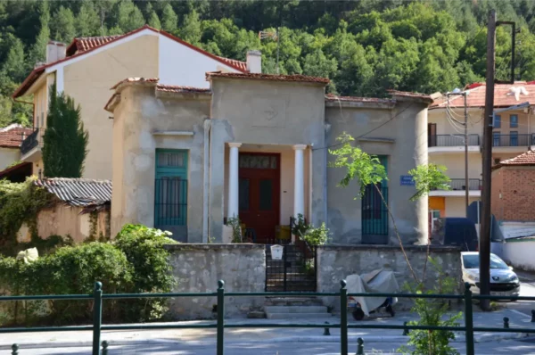 Charming building with red accents and green foliage in Florina, Greece, showcasing local architecture amidst a serene backdrop.
