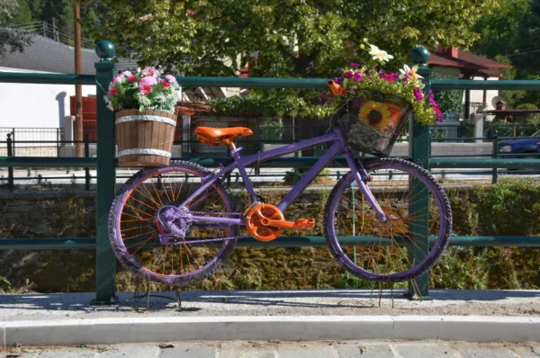A vibrant purple bicycle adorned with colorful flowers rests on a railing by the water in Florina, Greece.