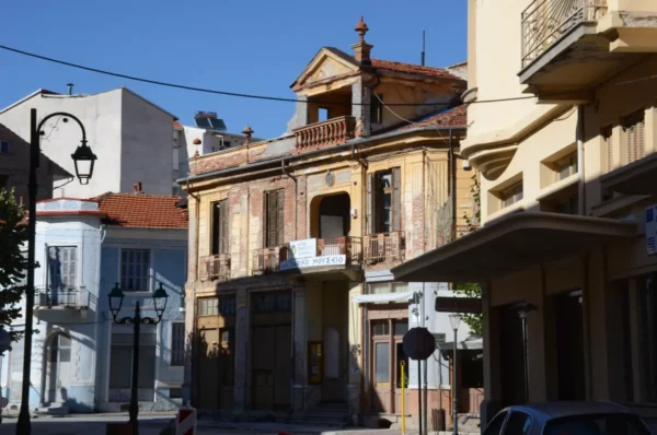 Historic architecture with faded colors and balconies lines the street in Florina, Greece, under a clear blue sky.