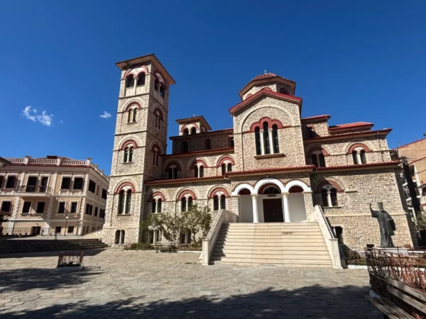 Stunning stone architecture with a bell tower stands on a sunlit square in Florina, Greece, against a clear blue sky.
