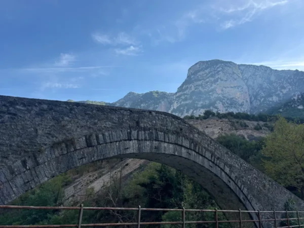 Politsa Bridge over the Arachthos River in Tzoumerka — single stone arch with mountains behind.
