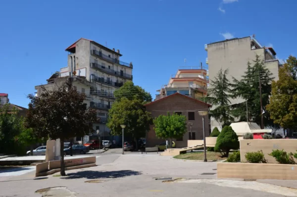 Sunny Grevena city in Greece showcases a vibrant square surrounded by diverse architecture and lush greenery.