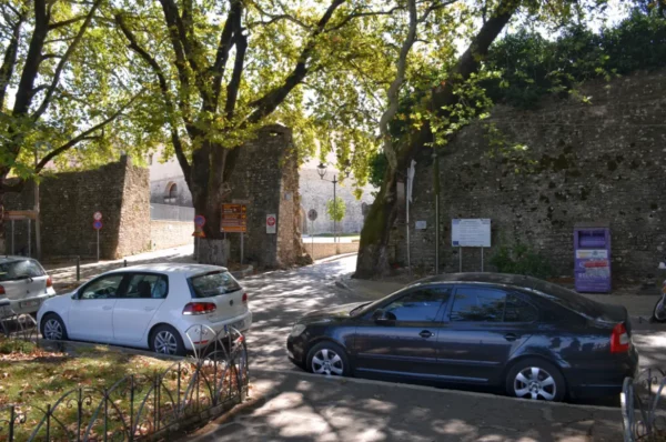 Historic stone walls framed by lush trees line the streets of Ioannina, Greece, with parked cars adding to the urban landscape.