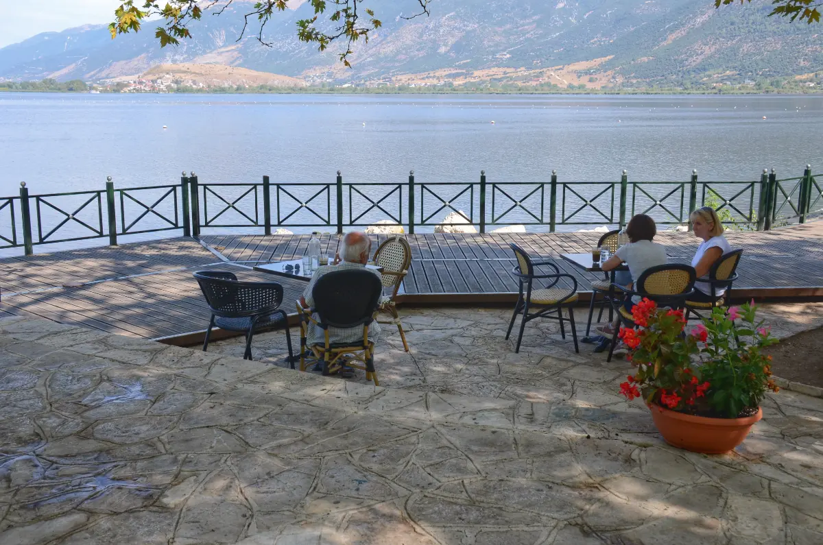 outdoor café by Lake Pamvotida with people sitting at tables and mountains in the background, Ioannina, Greece