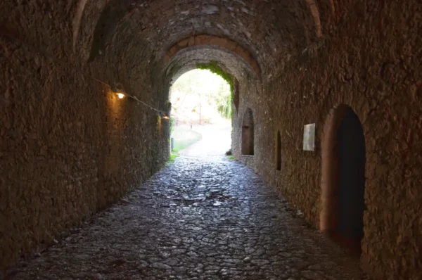 Stone archway leading to a sunlit path in Ioannina, Greece, showcasing textures of ancient walls and cobblestone flooring.