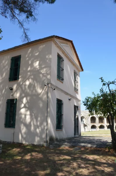 Historic white building with green shutters, surrounded by trees and grass in Ioannina, Greece, under a clear blue sky.