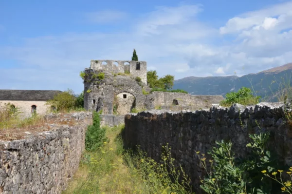 Ruins and lush greenery frame the historic fortress structure in Ioannina, Greece, against a backdrop of mountains and blue sky.