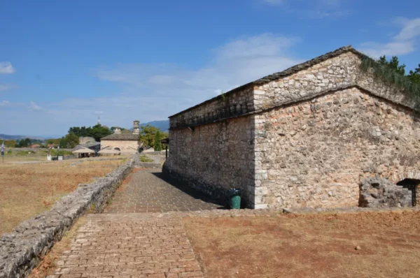 Stone walls and pathways lead through the historic site in Ioannina, Greece, with clear blue skies above.