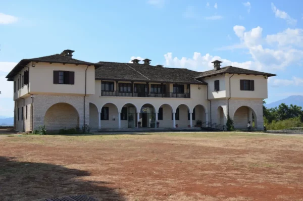 Historic building with arched entrances and large windows in Ioannina city, Greece, surrounded by a clear blue sky and grassy landscape.