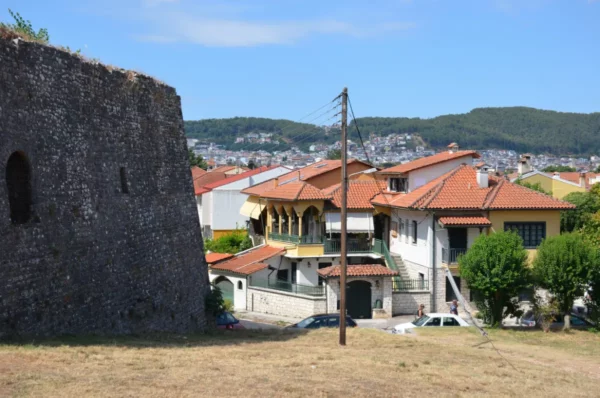 Stone wall structures contrast with colorful rooftops and green hills in Ioannina, Greece, under a clear blue sky.