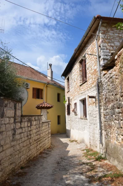 Charming stone alleyway lined with traditional houses in Ioannina, Greece, under a blue sky with scattered clouds.