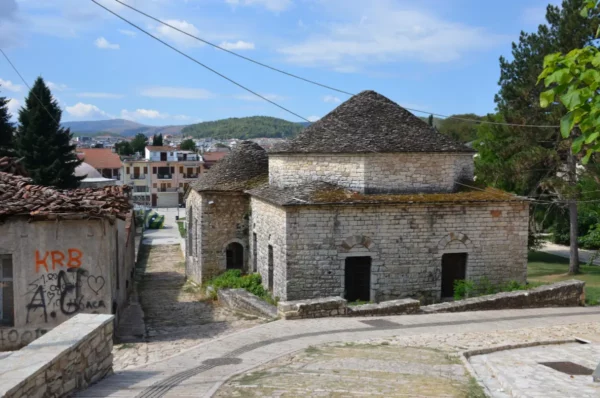 Historic stone buildings with round roofs and lush greenery in the charming streets of Ioannina, Greece. Clear blue sky enhances the scene.