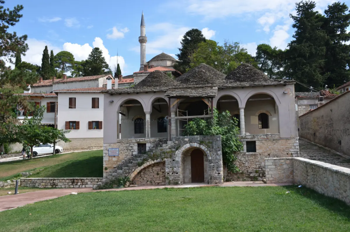 Ottoman Library at Its Kale in Ioannina Castle, a historic stone building with arches, tiled roof, and the minaret of Aslan Pasha Mosque rising in the background, Ioannina, Greece