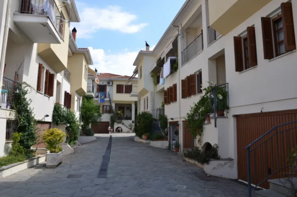 Charming street lined with white buildings and wooden shutters in Ioannina, Greece, adorned with greenery and a clear blue sky.