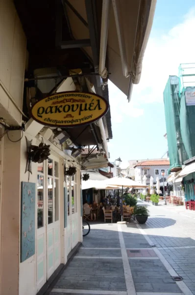 Charming street scene in Ioannina, Greece, featuring a cozy restaurant sign, outdoor seating, and vibrant blue skies.
