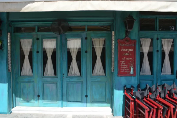 Charming turquoise facade with white curtains and vintage signage, showcasing a vibrant cafe in Ioannina, Greece.