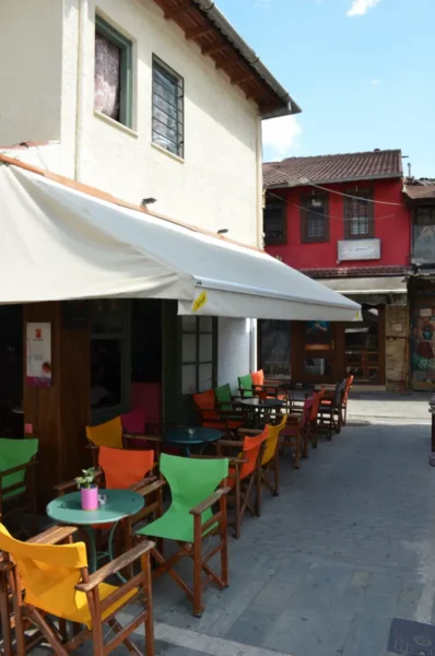 Colorful chairs line the outdoor seating area of a café in Ioannina, Greece, under a white awning against vibrant buildings.